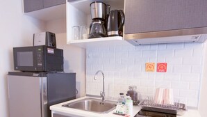 Una cocina compacta con microondas integrado, refrigerador, pileta de acero inoxidable y cafetera sobre la encimera.