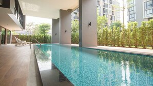 Una piscina con agua cristalina azul, rodeada por una terraza de madera y sillones de descanso.