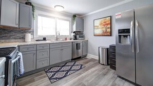 A modern kitchen with grey cabinets, stainless steel appliances, and a patterned rug. - River District Retreat—Walk to Downtown Belmont! (Belmont)