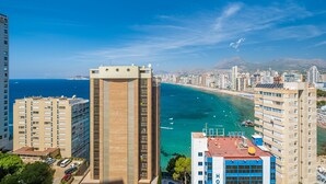 Un hotel moderno con vista su una città costiera, con una visuale chiara sul mare e sulle montagne in lontananza.