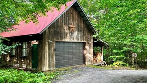A rustic wooden barn with a red roof, a garage door, and a star decoration on the wall. - Peaceful Family Retreat – Spacious 4BR Home - 5 acres of forest (Inlet)