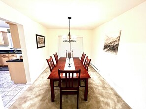 Un comedor con una larga mesa de madera, seis sillas, una araña y un cuadro en la pared.