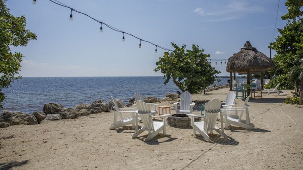 A beach setting with white lounge chairs, a thatched-roof structure, and a string of lights. - Kawama 3 bedroom townhouse--2 heated pools, marina, tennis, lagoon & much more! (Key Largo)