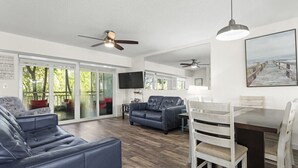 A modern living room with a sofa, a dining table with chairs, a ceiling fan, and a TV. - Kawama 3 bedroom townhouse--2 heated pools, marina, tennis, lagoon & much more! (Key Largo)