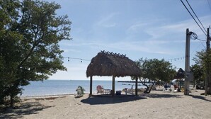 A beach with a thatched-roof structure, beach chairs, and a view of the sea. - Kawama 3 bedroom townhouse--2 heated pools, marina, tennis, lagoon & much more! (Key Largo)
