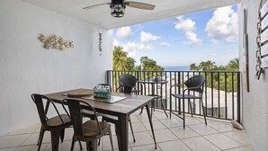 A balcony with a table and chairs, a ceiling fan, and a view of the ocean.