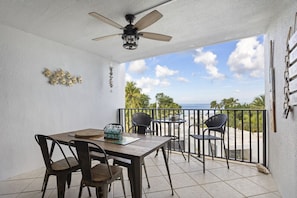 A balcony with a table and chairs, a ceiling fan, and a view of the ocean. - Gorgeous Moon Bay Condo Heated Pool Beach (Key Largo)