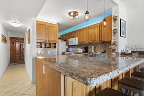 A kitchen with wooden cabinets, granite countertops, and pendant lighting. - Gorgeous Moon Bay Condo Heated Pool Beach (Key Largo)