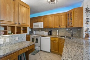A kitchen with wooden cabinets, granite countertops, a microwave, a stove, a dishwasher, and a sink.