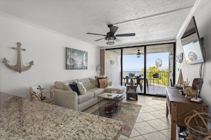 A living room with a sofa, coffee table, and a ceiling fan. There is a balcony with a view of the ocean. - Gorgeous Moon Bay Condo Heated Pool Beach (Key Largo)