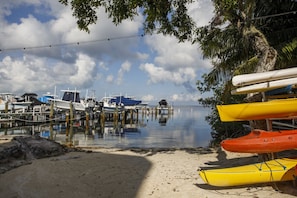 A marina with boats docked, a sandy beach, and a palm tree. - Gorgeous Moon Bay Condo Heated Pool Beach (Key Largo)