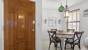 A dining area with a wooden table and four chairs, a wooden door, and a hanging light fixture.