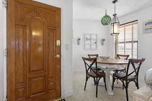 A dining area with a wooden table and four chairs, a wooden door, and a hanging light fixture. - Gorgeous Moon Bay Condo Heated Pool Beach (Key Largo)