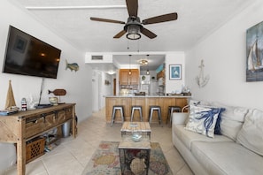A living room with a ceiling fan, a television, a wooden coffee table, and a sofa with a decorative pillow. - Gorgeous Moon Bay Condo Heated Pool Beach (Key Largo)