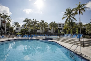 A swimming pool with blue lounge chairs and palm trees, surrounded by a building with balconies. - Gorgeous Moon Bay Condo Heated Pool Beach (Key Largo)