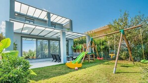 A modern house with a patio, a swing set, and a green slide. - Alyona Villa | Private Pool, Garden & Playground (Skines)