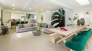 A modern living room with a sofa, coffee table, and a dining area with a long table and chairs. - Alyona Villa | Private Pool, Garden & Playground (Skines)