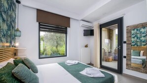 A modern bedroom with a large bed, green bedding, a view of greenery outside, a sliding glass door, and a mounted TV. - Alyona Villa | Private Pool, Garden & Playground (Skines)
