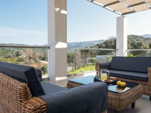Un balcón con mobiliario de mimbre, una mesa de vidrio y vistas al campo.