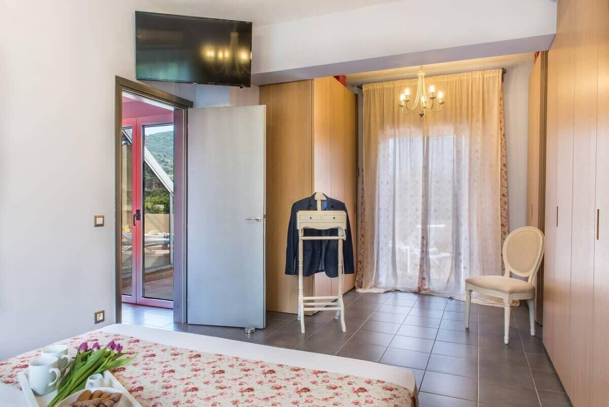 A bedroom with a bed, a chair, a wardrobe, a television, and a window with curtains.