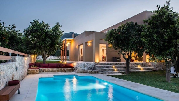 Una casa moderna con piscina, mobiliario de exterior y un muro de piedra.