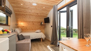 Una habitación compacta con una cama, un pequeño rincón de descanso, una mesa de comedor y un televisor fijado a la pared.