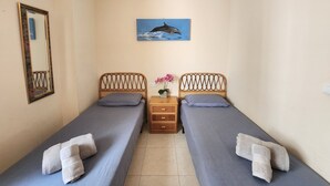 Ein kleines, sauberes Zimmer mit zwei Einzelbetten, einem Spiegel, einem kleinen Tisch mit Blumen und einem Bild von einem Delfin an der Wand.