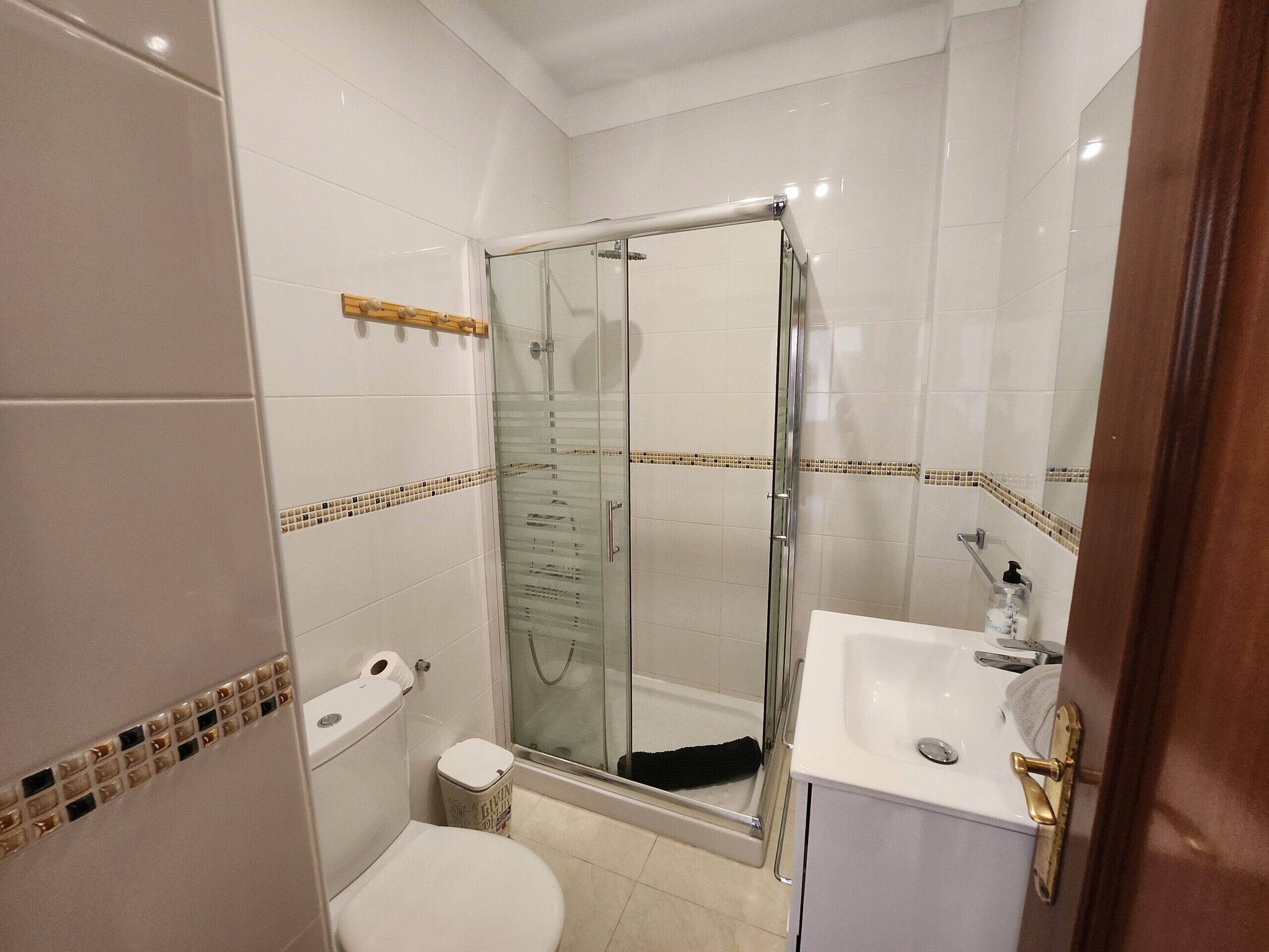 Une salle de bain avec une douche à parois de verre, un lavabo blanc avec un robinet doré et des toilettes avec un abattant beige.