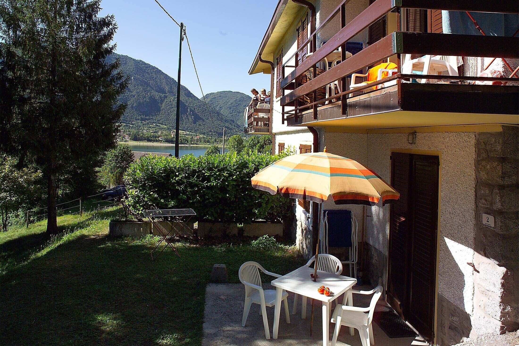 A balcony with a view of a lake and mountains, a table with chairs, and an umbrella.
