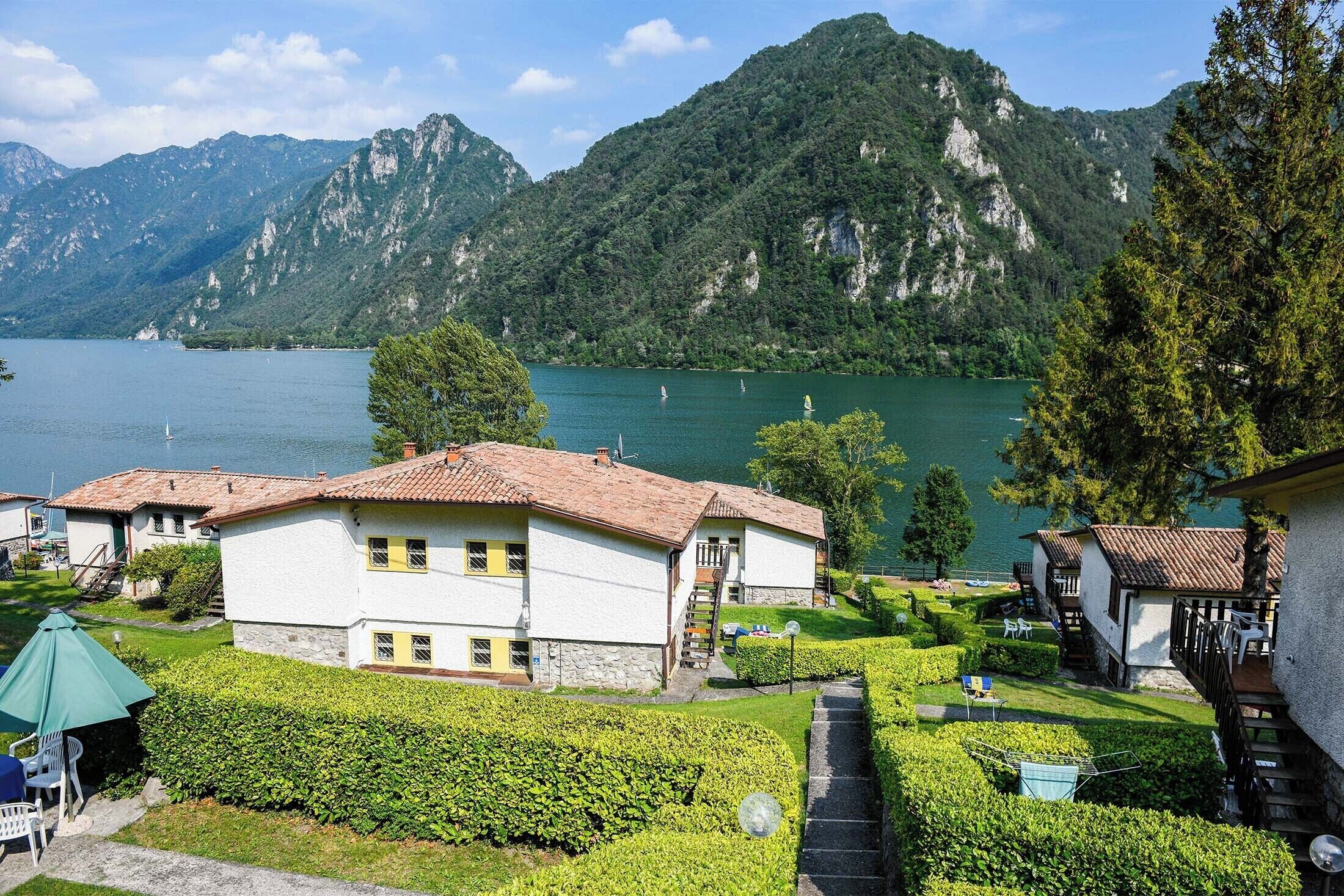 Une propriété au bord du lac, avec des bâtiments blancs, un jardin bien entretenu et une vue sur le lac et les montagnes.