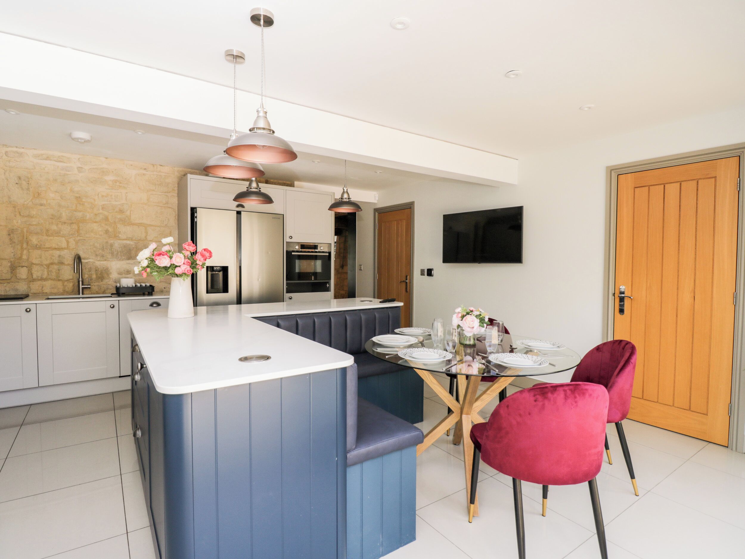A modern kitchen with a central island, stainless steel appliances, and a dining area with a glass table and red chairs.