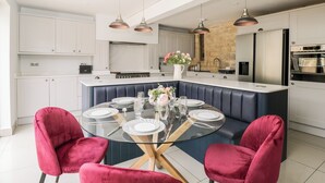 Una cocina moderna con una isla central, armarios blancos y un comedor con mesa de vidrio y sillas rojas.