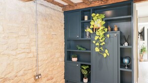 Una habitación con vigas de madera a la vista, una pared de piedra y un estante azul oscuro con plantas en macetas y objetos decorativos.