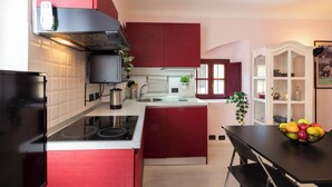 A modern kitchen with red cabinetry, a black stove, and a dining area with a fruit bowl. - notaMI - Forcella Fashion District  (Milan)