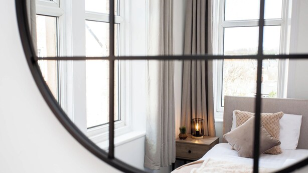 Un dormitorio con cama, mesita de noche, lámpara y cortinas.
