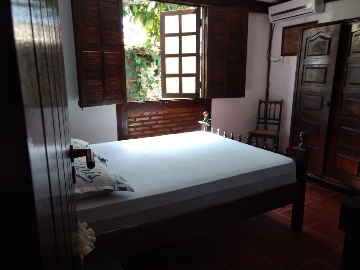 A bedroom with a bed, wooden shutters, a brick wall, and a door.