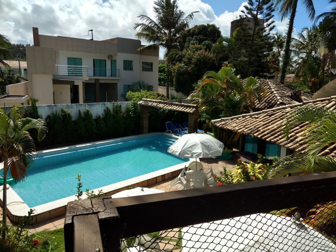 A swimming pool with a white umbrella, surrounded by palm trees and a building with a balcony.