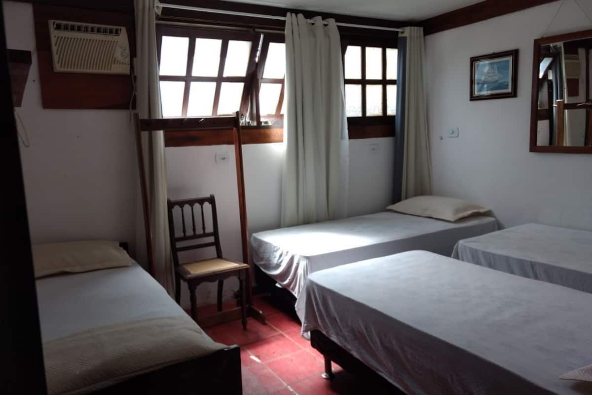 Ein Zimmer mit zwei Einzelbetten, einem Sessel, einer Heizung und einem Fenster mit Vorhängen.