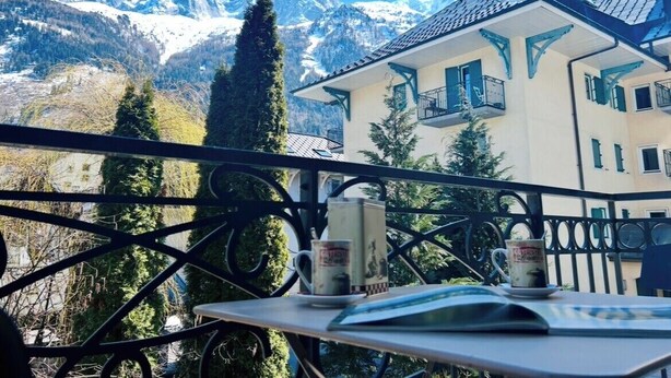 A balcony with a mountain view, a table with a book and two mugs, and a building with balconies. - Flat with parking and balcony in Centre (Chamonix-Mont-Blanc)