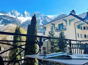 Un balcon avec vue sur la montagne, une table avec un livre et deux tasses, et un immeuble doté de balcons.