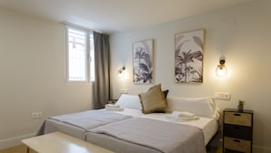 Ein Hotelzimmer mit zwei Betten, einem kleinen Tisch, einem Nachttisch mit Pflanze und Bildern an den Wänden.