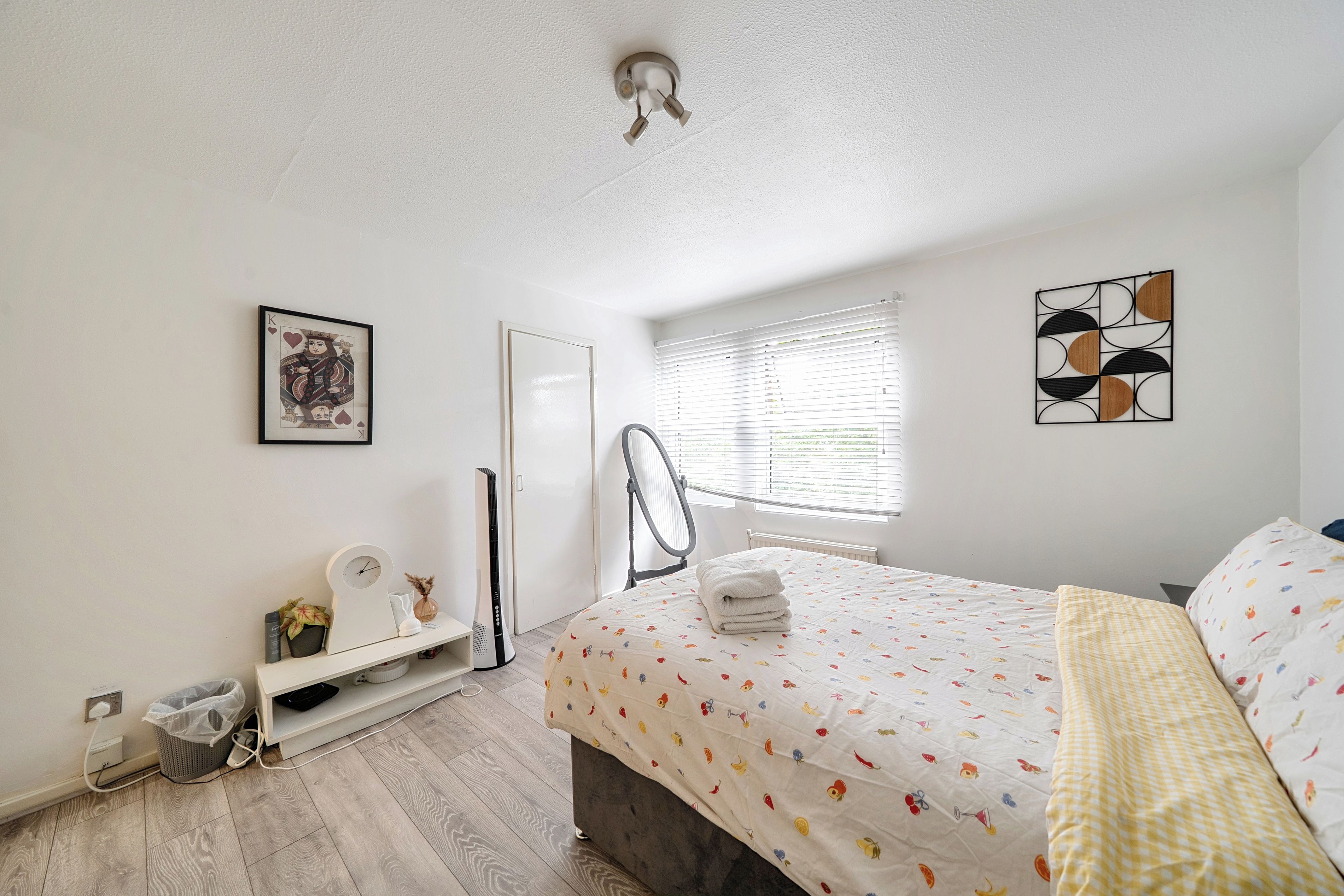 A bedroom with a bed, a radiator, a window with blinds, a wall-mounted artwork, and a ceiling light fixture.