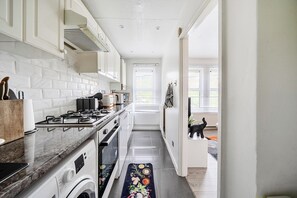 A narrow kitchen with white cabinetry, a stove, and a washing machine. - Central London Apt - Sleeps 3 - Street Parking (London)