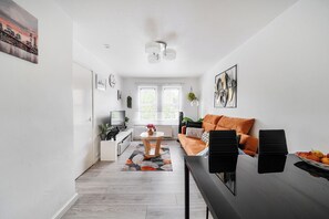 A modern living room with a sofa, coffee table, and a dining area with chairs. - Central London Apt - Sleeps 3 - Street Parking (London)