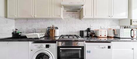 Une cuisine compacte avec des meubles blancs, un four encastré, un lave-linge et un four à micro-ondes.