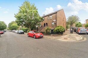 A residential street with parked cars, a red car in the foreground, and a brick house with a sign reading 'Warrender Road.' - Central London Apt - Sleeps 3 - Street Parking (London)