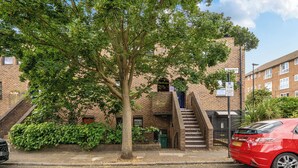 A red car parked in front of a brick building with a tree in the foreground. - Central London Apt - Sleeps 3 - Street Parking (London)