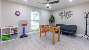 Una habitación con mesa de futbolín, aro de baloncesto, sofá, perchero y estantería.