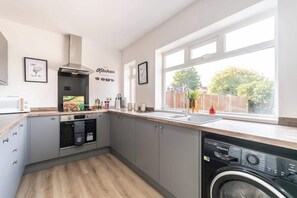 A modern kitchen with grey cabinets, a built-in oven, a dishwasher, and a large window offering a view of the outdoors.