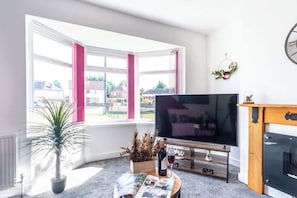 A living room with a large flat-screen TV, a potted plant, a wine bottle, and a magazine on a coffee table.
